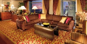 grosses edles luxuriöses und modernes wohnzimmer im hotel mit einer grossen couch mit muster auf dem tisch eine schale und zwei hände aus stein als dekoration am boden ein schöner asiatischer teppich und an der seite zwei grosse panorama fenster für tolle